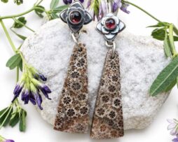 Nahaufnahme von handgemachten langen Blumen-Ohrringen aus 925 Sterling Silber mit detaillierten Blüten-Elementen, roten Hessonit Granat Steinen und gemustertem Fossil Korallen Achat.