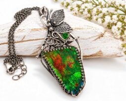 Handgefertigter Ammolith-Silberanhänger mit Schmetterling-Design und grünem Chromdiopsid liegt neben einer Kette auf hellem Holz.