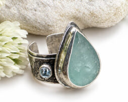 Botanischer Silberring mit dreieckigem Aquamarin und blauem Topas neben einer Blume.